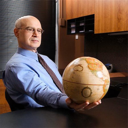 Caucasian middle-aged businessman sitting at desk in office holding globe. Stock Photo - Budget Royalty-Free & Subscription, Code: 400-04954764