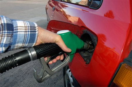 Close up of the hand of a motorist, filling his car with unleaded petrol on a garage forecourt. Beyond is the empty forecourt, but reflected in the car's bodywork is a housing estate and trees. Stock Photo - Budget Royalty-Free & Subscription, Code: 400-04978573