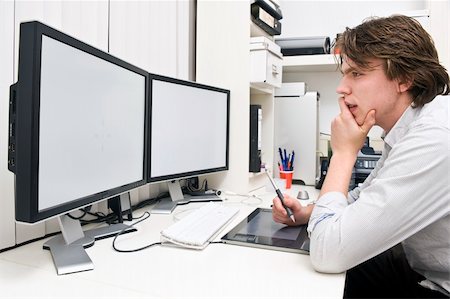 A young man at work behind a dual monitor work station in a design studio office environment Stock Photo - Budget Royalty-Free & Subscription, Code: 400-05095441