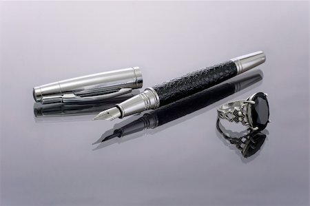 Presentable luxury pen with the opened tip and elegant austere silver ring with a black jewel.  Objects lie on a glass surface and reflected from it. Stock Photo - Budget Royalty-Free & Subscription, Code: 400-05097027
