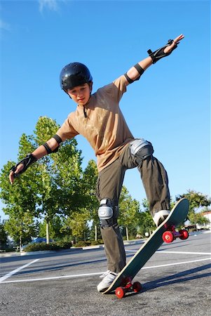simsearch:400-05737917,k - Teenage boy balancing on a skateboard in a parking lot on a sunny day with blue sky and trees in the background. Stock Photo - Budget Royalty-Free & Subscription, Code: 400-05119974