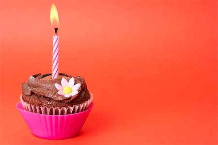 simsearch:400-04764403,k - Miniature chocolate cupcake with icing, decorative flower and birthday candle on red background with copy space Stock Photo - Budget Royalty-Free & Subscription, Code: 400-05125457