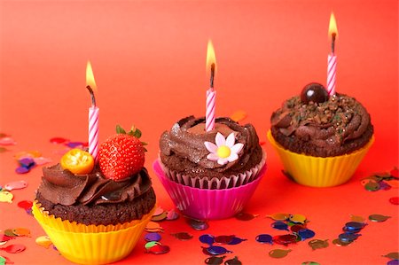 simsearch:400-04764403,k - Miniature chocolate cupcakes with icing, decorative flower, strawberry and birthday candles on red background with decorations Stock Photo - Budget Royalty-Free & Subscription, Code: 400-05141013