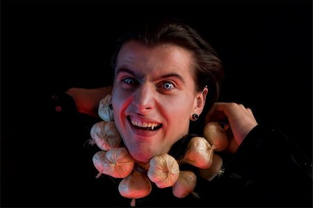 Funny vampire with scary eyes suffocated from being choked by garlic, isolated on black background Stock Photo - Budget Royalty-Free & Subscription, Code: 400-05167485