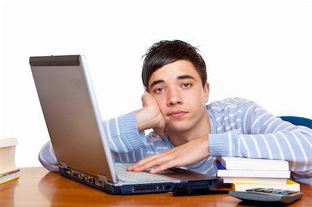 simsearch:400-04704759,k - Young teenager is sitting on desk and learns with computer and books for his exams. He looks frustrated into camera. Isolated on white. Stock Photo - Budget Royalty-Free & Subscription, Code: 400-05200069