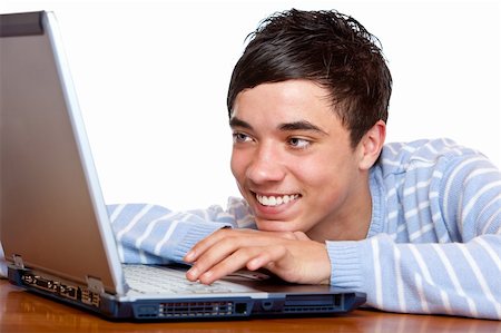 simsearch:400-04704759,k - Young teenager is sitting on desk, is surfing on the internet and looking happy on laptop display. Isolated on white. Stock Photo - Budget Royalty-Free & Subscription, Code: 400-05200070