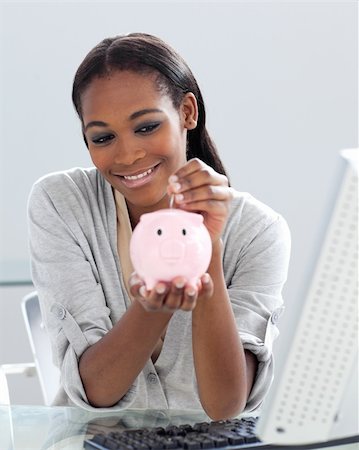 simsearch:400-04184165,k - Assertive Afro-american businesswoman saving money in a piggybank at her desk Stock Photo - Budget Royalty-Free & Subscription, Code: 400-05224415
