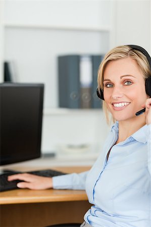 Close up of a smiling blonde businesswoman with headset working with computer looking into camera in her office Stock Photo - Budget Royalty-Free & Subscription, Code: 400-05345295