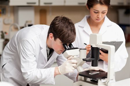simsearch:400-05669968,k - Scientist looking in a microscope while his colleague is taking notes in a laboratory Stock Photo - Budget Royalty-Free & Subscription, Code: 400-05669954