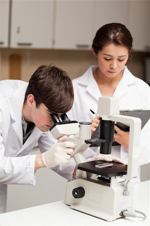 simsearch:400-05669968,k - Portrait of a scientist looking in a microscope while his coworker is taking notes in a laboratory Stock Photo - Budget Royalty-Free & Subscription, Code: 400-05669956