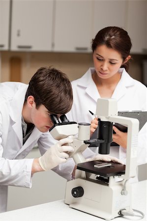 simsearch:400-05669968,k - Portrait of a scientist looking in a microscope while his colleague is taking notes in a laboratory Stock Photo - Budget Royalty-Free & Subscription, Code: 400-05669957