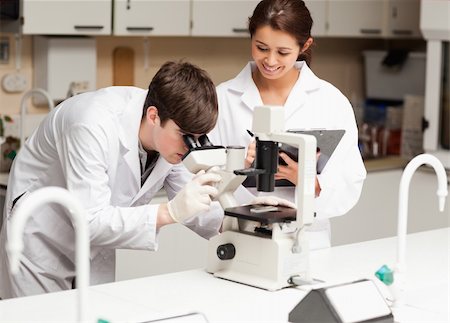 simsearch:400-05669968,k - Scientist looking in a microscope while his coworker is taking notes in a library Stock Photo - Budget Royalty-Free & Subscription, Code: 400-05669959