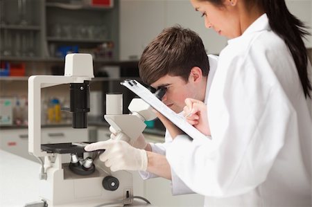 simsearch:400-05669968,k - Scientist looking in a microscope while his coworker is writing in a laboratory Stock Photo - Budget Royalty-Free & Subscription, Code: 400-05669966