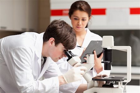 simsearch:400-05669968,k - Scientist looking in a microscope while his colleague is writing in a laboratory Stock Photo - Budget Royalty-Free & Subscription, Code: 400-05669968