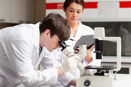 simsearch:400-05669968,k - Science student looking in a microscope while his classmate is writing in a library Stock Photo - Budget Royalty-Free & Subscription, Code: 400-05669970