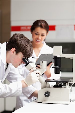 simsearch:400-05669968,k - Portrait of a science student looking in a microscope while his classmate is writing in a laboratory Stock Photo - Budget Royalty-Free & Subscription, Code: 400-05669971