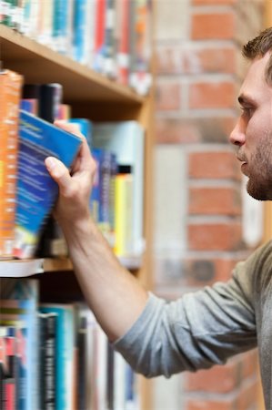 simsearch:400-05669803,k - Portrait of a male student picking a book in a library Stock Photo - Budget Royalty-Free & Subscription, Code: 400-05678157