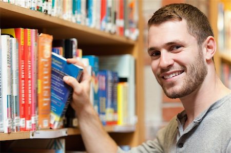 simsearch:400-07337983,k - Smiling male student picking a book in a library Stock Photo - Budget Royalty-Free & Subscription, Code: 400-05678159