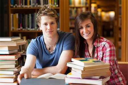 simsearch:400-05669755,k - Smiling students surrounded by books in a library Photographie de stock - Aubaine LD & Abonnement, Code: 400-05678171