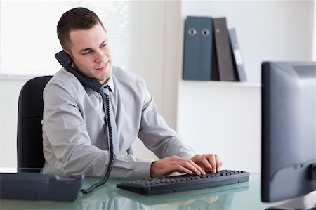 simsearch:400-05710264,k - Young businessman on the telephone and typing on his computer Stock Photo - Budget Royalty-Free & Subscription, Code: 400-05709699