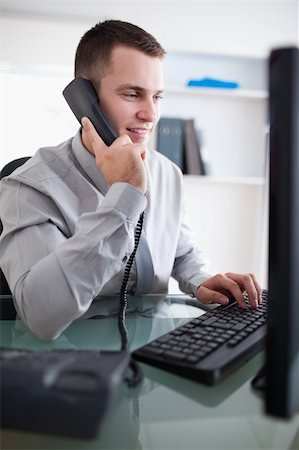 simsearch:400-05710264,k - Young businessman talking to costumer on the phone while using his computer Stock Photo - Budget Royalty-Free & Subscription, Code: 400-05709707