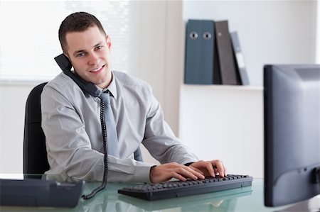 simsearch:400-05710264,k - Smiling young businessman on the phone and writing on his computer Stock Photo - Budget Royalty-Free & Subscription, Code: 400-05709700