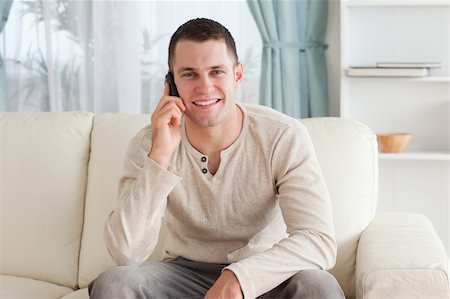 simsearch:400-04212823,k - Handsome man making a phone call while sitting on a couch in his living room Stock Photo - Budget Royalty-Free & Subscription, Code: 400-05715329