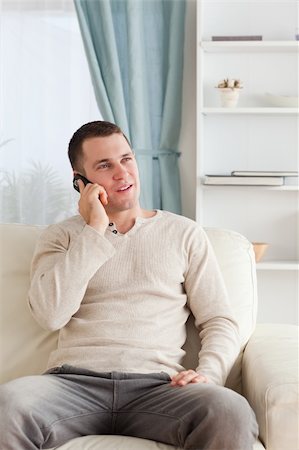 simsearch:400-04212823,k - Portrait of a young man on the phone while sitting on his sofa in his living room Stock Photo - Budget Royalty-Free & Subscription, Code: 400-05715320