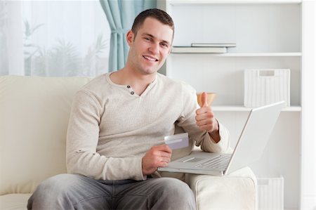 face to internet technology - Happy man shopping online with the thumb up in his living room Photographie de stock - Aubaine LD & Abonnement, Code: 400-05715535