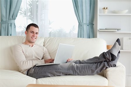 simsearch:400-04412244,k - Smiling man relaxing with a laptop in his living room Stock Photo - Budget Royalty-Free & Subscription, Code: 400-05715585