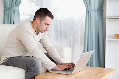 simsearch:400-04412244,k - Young man typing on his laptop in his living room Stock Photo - Budget Royalty-Free & Subscription, Code: 400-05715604