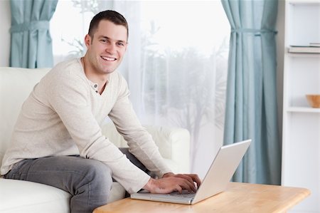 simsearch:400-04412244,k - Smiling man typing on his laptop in his living room Stock Photo - Budget Royalty-Free & Subscription, Code: 400-05715605