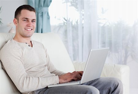 simsearch:400-04412244,k - Happy man typing on his notebook in his living room Stock Photo - Budget Royalty-Free & Subscription, Code: 400-05715608