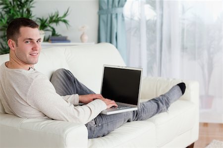 simsearch:400-04412244,k - Man lying on his couch with a laptop while looking at the camera Stock Photo - Budget Royalty-Free & Subscription, Code: 400-05715644