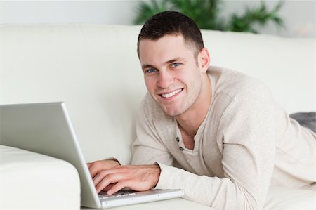 simsearch:400-04412244,k - Man lying on a sofa with a laptop while looking at the camera Stock Photo - Budget Royalty-Free & Subscription, Code: 400-05715655