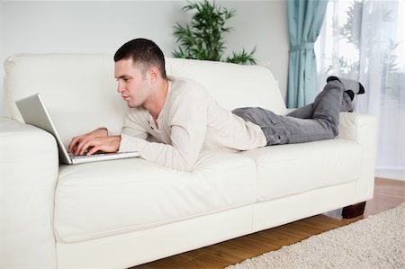 simsearch:400-04412244,k - Handsome man lying on a couch using a laptop in his living room Stock Photo - Budget Royalty-Free & Subscription, Code: 400-05715664