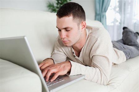 simsearch:400-04412244,k - Focused man lying on a sofa using a laptop in his living room Stock Photo - Budget Royalty-Free & Subscription, Code: 400-05715660