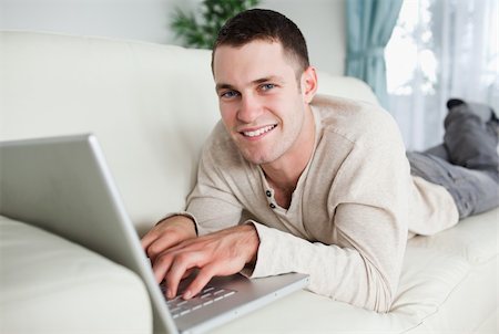 simsearch:400-04412244,k - Smiling man lying on a couch with a laptop while looking at the camera Stock Photo - Budget Royalty-Free & Subscription, Code: 400-05715661