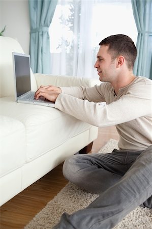 simsearch:400-04412244,k - Portrait of a smiling man sitting on a carpet while using a laptop in his living room Stock Photo - Budget Royalty-Free & Subscription, Code: 400-05715674