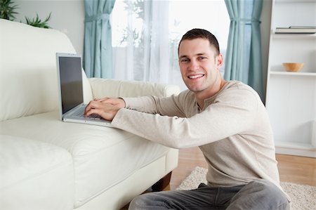 simsearch:400-04412244,k - Smiling man sitting on a carpet with a laptop in his living room Stock Photo - Budget Royalty-Free & Subscription, Code: 400-05715676
