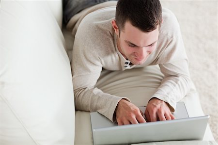 simsearch:400-04412244,k - Young man lying on a couch to use a laptop in his living room Stock Photo - Budget Royalty-Free & Subscription, Code: 400-05715670