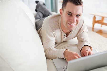 simsearch:400-04412244,k - Good looking man lying on a couch with a laptop while looking at the camera Stock Photo - Budget Royalty-Free & Subscription, Code: 400-05715691