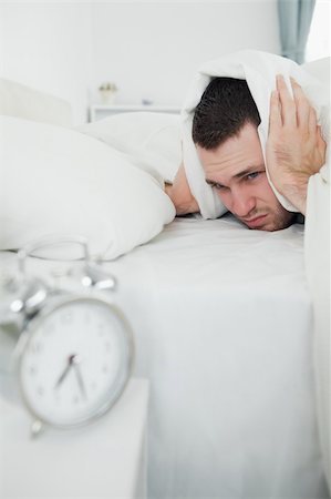 simsearch:6109-06194878,k - Portrait of an attractive man covering his ears with a duvet while his alarm is ringing in his bedroom Stock Photo - Budget Royalty-Free & Subscription, Code: 400-05737285