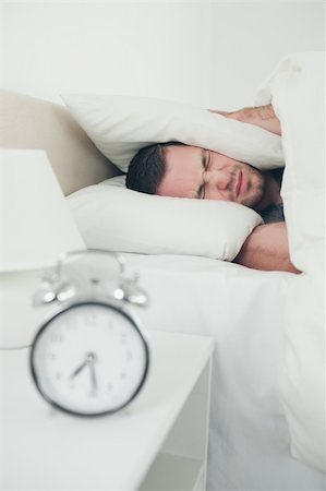 simsearch:6109-06194878,k - Portrait of a unhappy man covering his ears while his alarm clock is ringing in his bedroom Stock Photo - Budget Royalty-Free & Subscription, Code: 400-05737294