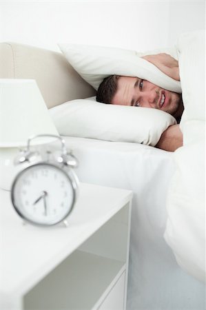 simsearch:6109-06194878,k - Portrait of a unhappy man covering his ears with a pillow while his alarm clock is ringing Stock Photo - Budget Royalty-Free & Subscription, Code: 400-05737354