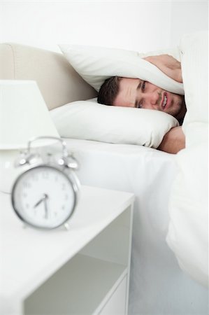 simsearch:6109-06194878,k - Portrait of an attractive man covering his ears with a pillow while his alarm clock is ringing Stock Photo - Budget Royalty-Free & Subscription, Code: 400-05737355