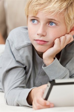 A young blond haired blue eyed boy child resting on his hands laying down on a sofa using tablet computer Stock Photo - Budget Royalty-Free & Subscription, Code: 400-05745191