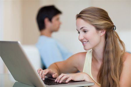 simsearch:400-04412244,k - Woman using a laptop while her fiance is sitting on a sofa in their living room Stock Photo - Budget Royalty-Free & Subscription, Code: 400-05746733