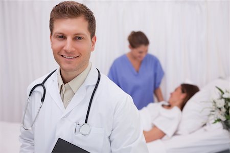 simsearch:400-05748252,k - Doctor standing in patients room with colleague and patient behind him Stock Photo - Budget Royalty-Free & Subscription, Code: 400-05748260