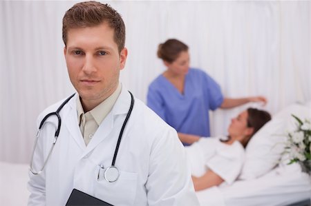 simsearch:400-05748252,k - Doctor standing in his patients room with patient and colleague behind him Stock Photo - Budget Royalty-Free & Subscription, Code: 400-05748261